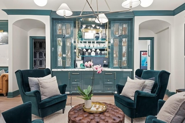 bar featuring arched walkways, crown molding, light wood finished floors, wet bar, and hanging light fixtures