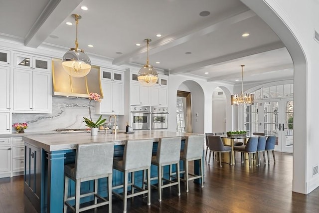 kitchen featuring beam ceiling, a center island with sink, white cabinets, and dark wood-type flooring