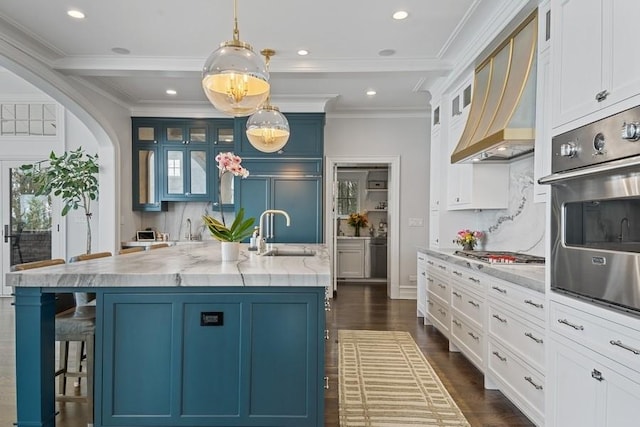 kitchen with a sink, premium range hood, stainless steel appliances, blue cabinets, and dark wood-style flooring