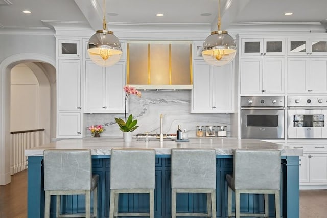 kitchen featuring backsplash, arched walkways, appliances with stainless steel finishes, white cabinets, and hanging light fixtures