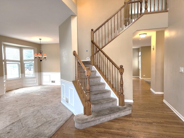 staircase featuring an inviting chandelier, wood finished floors, wainscoting, and a decorative wall