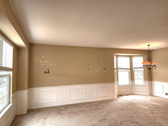 empty room with a wainscoted wall, light colored carpet, a chandelier, and a decorative wall