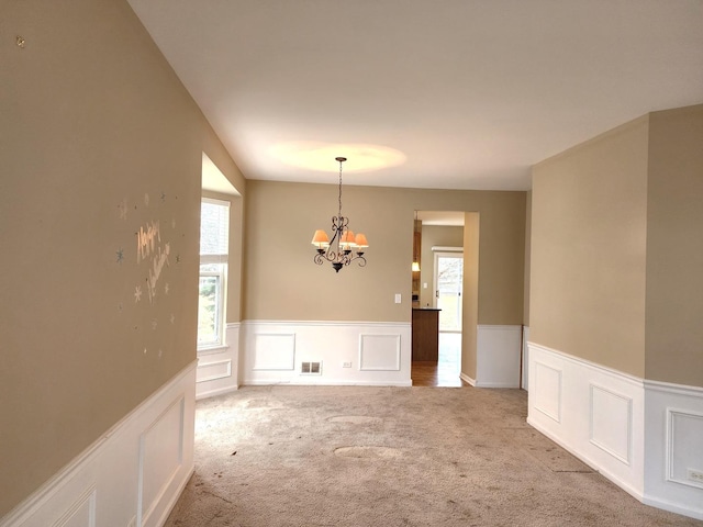 spare room with a wainscoted wall, visible vents, carpet floors, and a chandelier