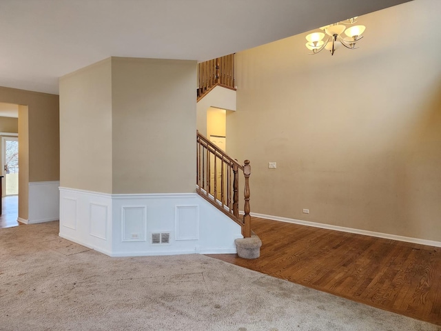 interior space with visible vents, carpet floors, wainscoting, a decorative wall, and a chandelier