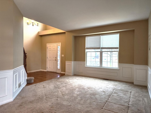 foyer featuring visible vents, carpet, wainscoting, a decorative wall, and stairs