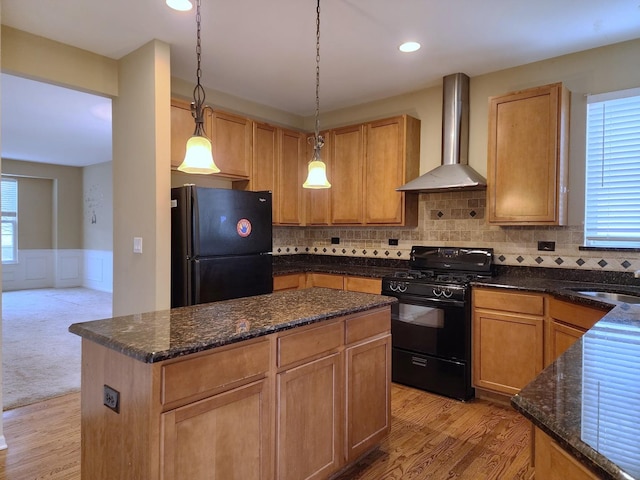 kitchen with a kitchen island, a sink, black appliances, wainscoting, and wall chimney exhaust hood