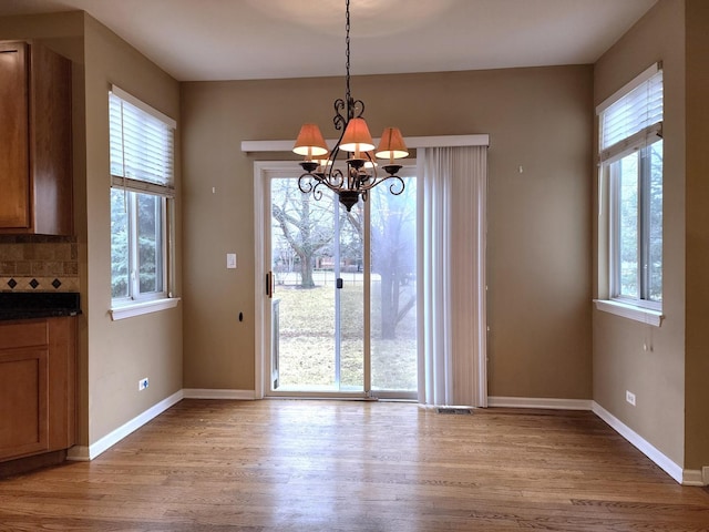 unfurnished dining area with an inviting chandelier, wood finished floors, and baseboards