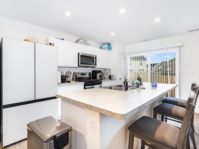 kitchen with visible vents, a sink, stainless steel appliances, white cabinetry, and a kitchen bar