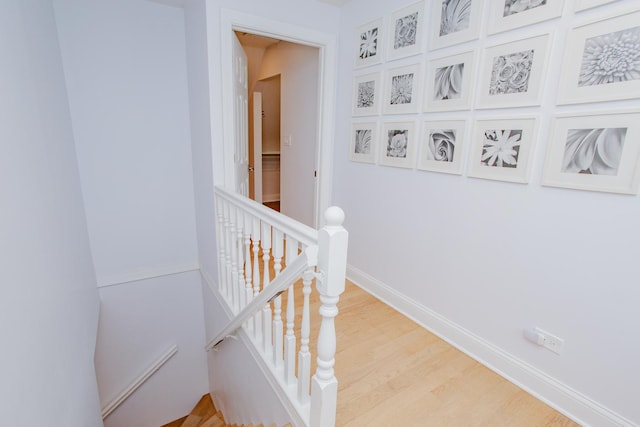 hall with light wood-type flooring, baseboards, and an upstairs landing