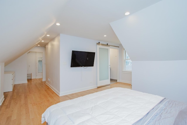 bedroom with vaulted ceiling, a barn door, light wood-type flooring, and recessed lighting