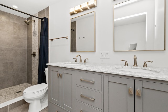 full bathroom with double vanity, tiled shower, a sink, and toilet