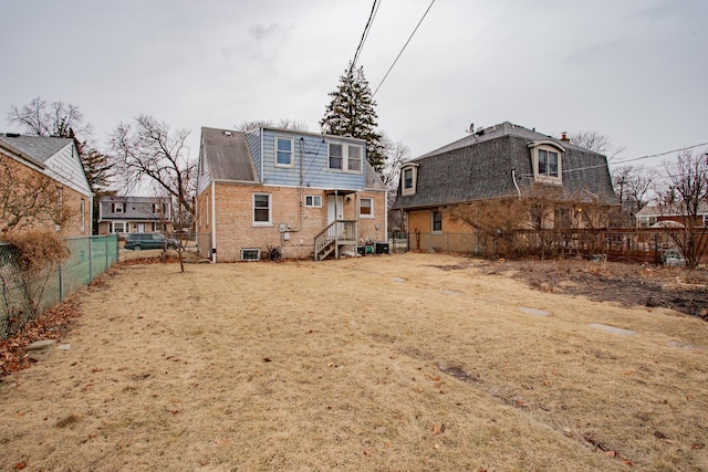 back of house featuring brick siding, fence, mansard roof, and roof with shingles