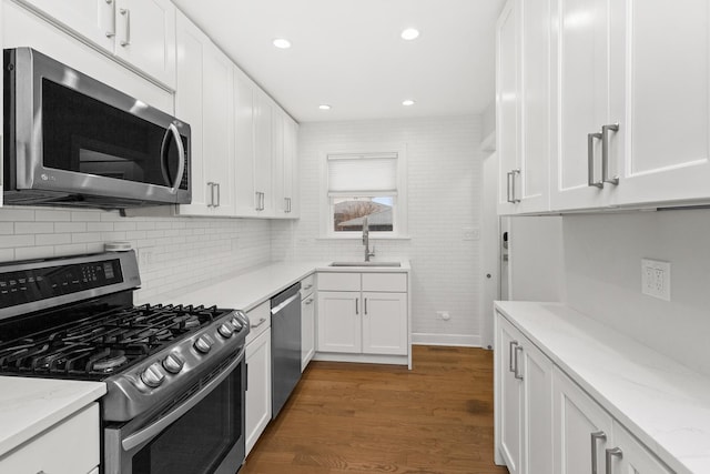 kitchen with stainless steel appliances, wood finished floors, a sink, and white cabinetry