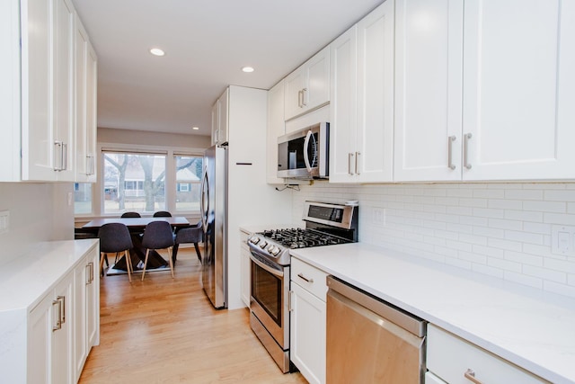 kitchen with appliances with stainless steel finishes, backsplash, white cabinetry, and light wood-style floors