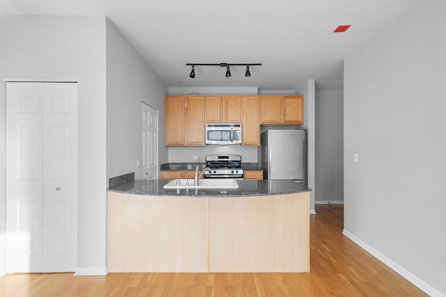 kitchen featuring stainless steel appliances, light wood-style flooring, a sink, dark stone counters, and a peninsula