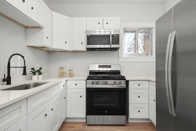 kitchen with appliances with stainless steel finishes, white cabinetry, light wood-style floors, and a sink