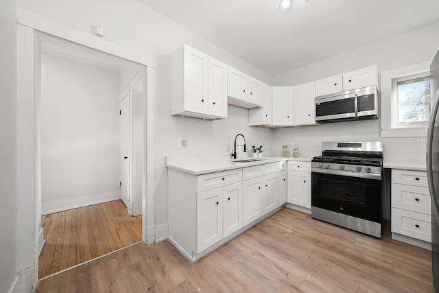 kitchen with light wood finished floors, light countertops, appliances with stainless steel finishes, white cabinets, and a sink