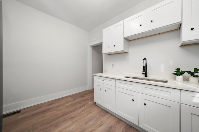 kitchen with visible vents, a sink, white cabinets, light wood finished floors, and baseboards