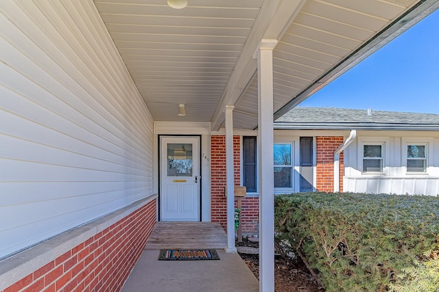 doorway to property with brick siding and a shingled roof