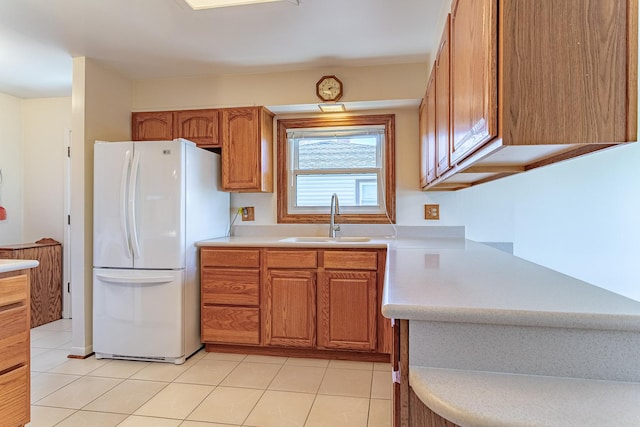 kitchen with brown cabinetry, freestanding refrigerator, light countertops, and a sink