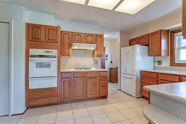 kitchen with brown cabinetry, white appliances, a warming drawer, and under cabinet range hood