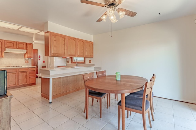 kitchen with tasteful backsplash, a peninsula, light countertops, under cabinet range hood, and stainless steel gas cooktop