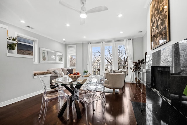 dining room featuring visible vents, ornamental molding, a high end fireplace, wood finished floors, and baseboards