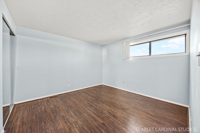 empty room with visible vents, a textured ceiling, baseboards, and wood finished floors