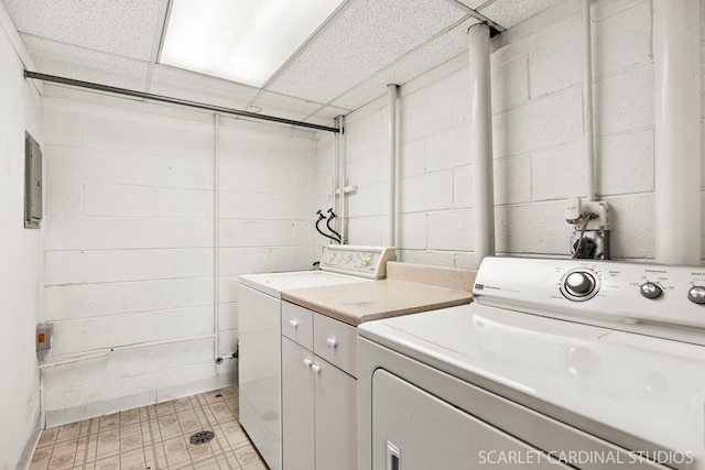 clothes washing area featuring washing machine and dryer, electric panel, cabinet space, and concrete block wall