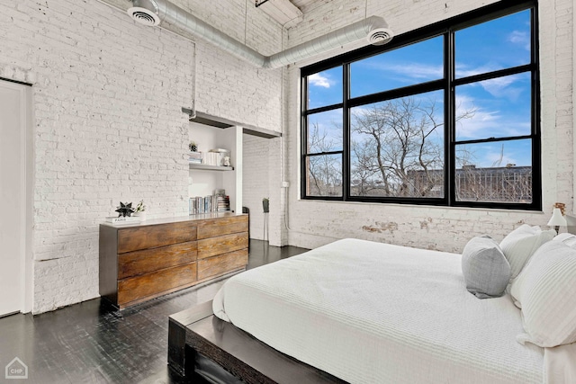 bedroom featuring dark wood-style flooring, visible vents, a towering ceiling, and brick wall