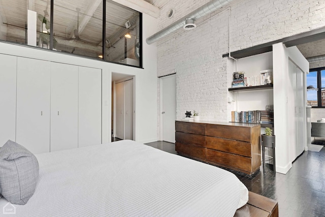 bedroom with brick wall, a high ceiling, and dark wood-type flooring