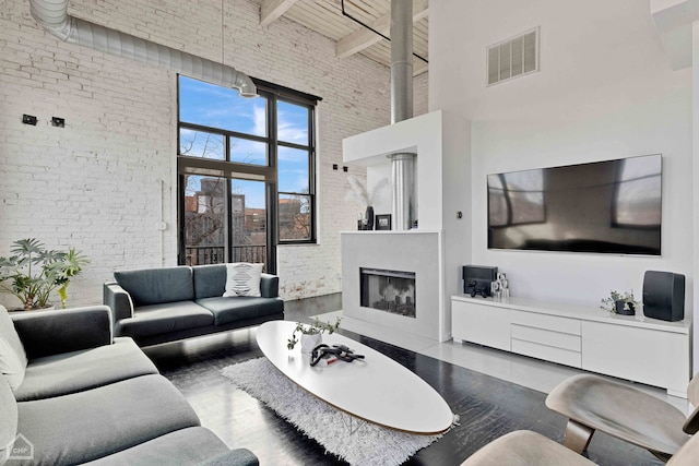 living area featuring a glass covered fireplace, visible vents, brick wall, and wood finished floors