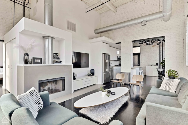 living area with dark wood finished floors, a fireplace, visible vents, a towering ceiling, and brick wall