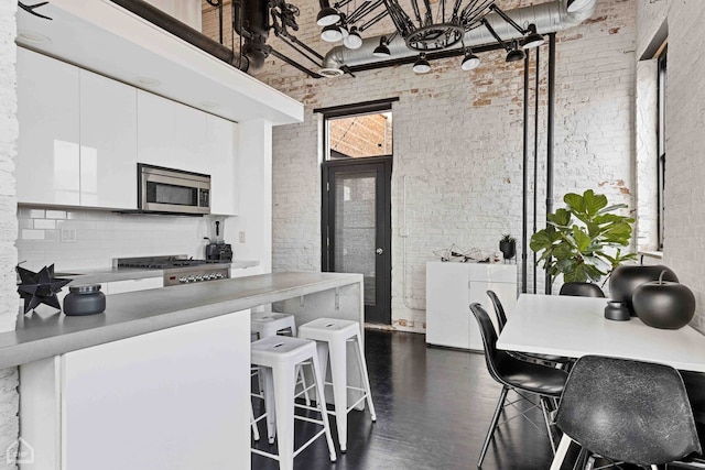 kitchen with brick wall, a high ceiling, and stainless steel microwave