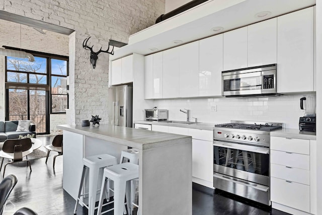 kitchen with stainless steel appliances, a towering ceiling, decorative backsplash, a sink, and a kitchen breakfast bar