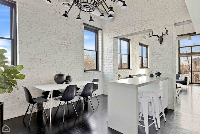 interior space featuring dark wood-type flooring, a wealth of natural light, a towering ceiling, and brick wall