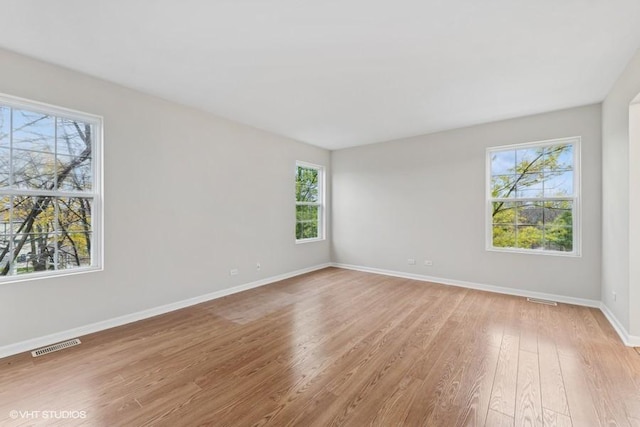 spare room with light wood-type flooring, visible vents, and baseboards