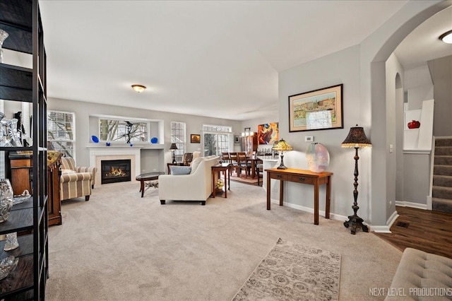 carpeted living room featuring a glass covered fireplace, arched walkways, baseboards, and stairs