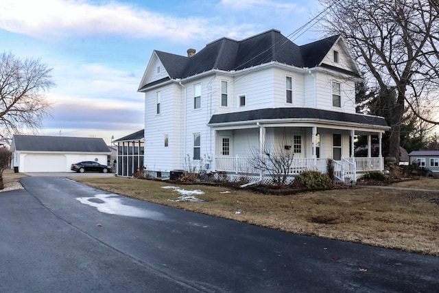 view of front of property featuring a garage, a chimney, a porch, and an outbuilding