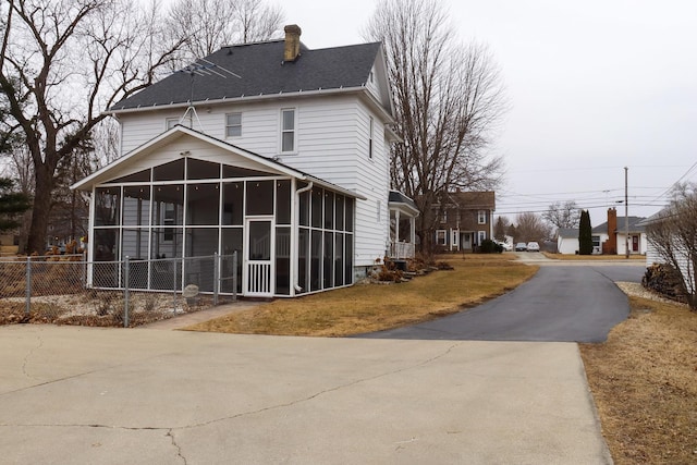 exterior space with a shingled roof, a sunroom, fence, and a chimney