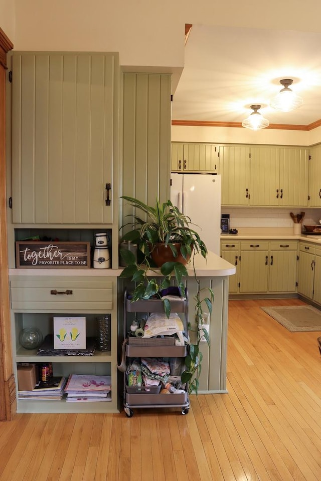 kitchen with light countertops, ornamental molding, freestanding refrigerator, and light wood-style floors