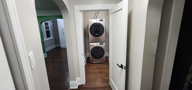 laundry room featuring arched walkways, stacked washer and dryer, laundry area, dark wood-style flooring, and baseboards