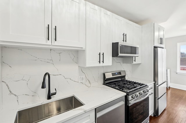 kitchen featuring light stone counters, stainless steel appliances, tasteful backsplash, white cabinetry, and a sink