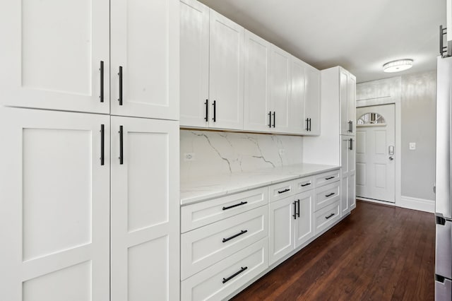 kitchen featuring dark wood-style flooring, decorative backsplash, white cabinets, light stone countertops, and baseboards