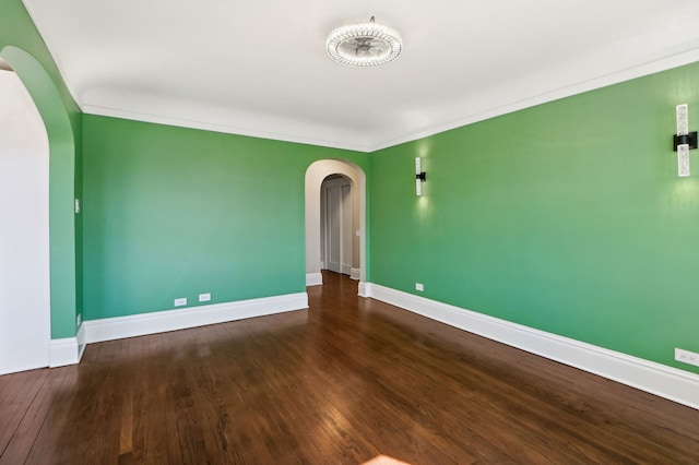 empty room featuring arched walkways, crown molding, wood finished floors, and baseboards