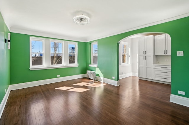 unfurnished bedroom with arched walkways, baseboards, ornamental molding, dark wood-style floors, and radiator heating unit