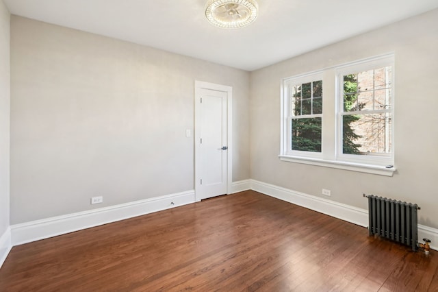 spare room with radiator heating unit, wood finished floors, and baseboards