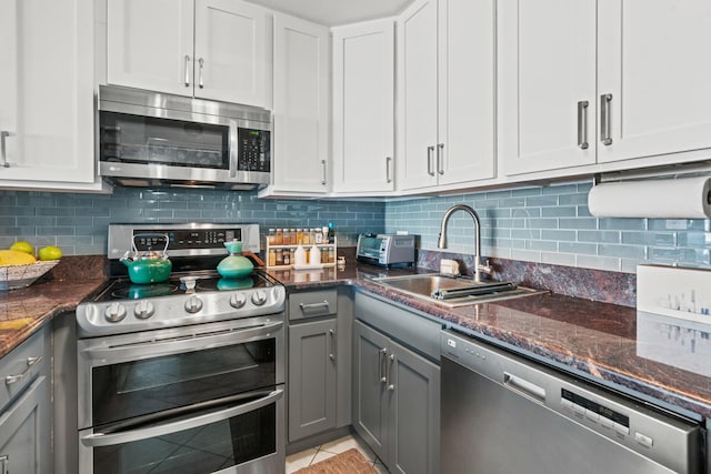 kitchen featuring gray cabinets, a sink, stainless steel appliances, dark stone counters, and decorative backsplash