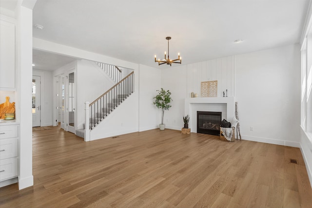 unfurnished living room with a notable chandelier, a glass covered fireplace, stairs, and light wood finished floors