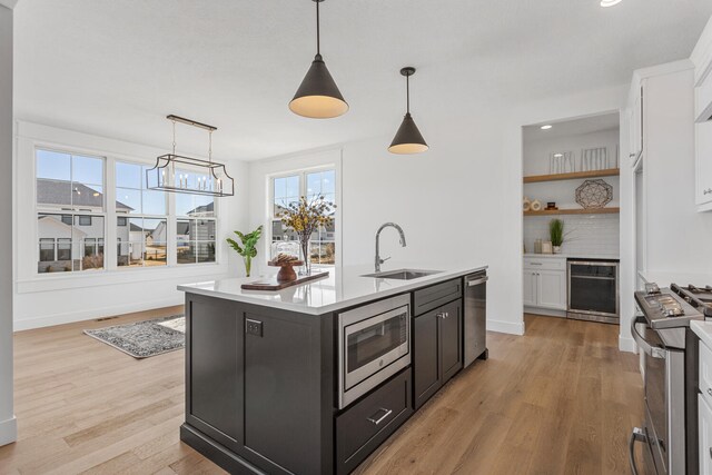 kitchen featuring beverage cooler, an island with sink, a sink, stainless steel appliances, and white cabinetry